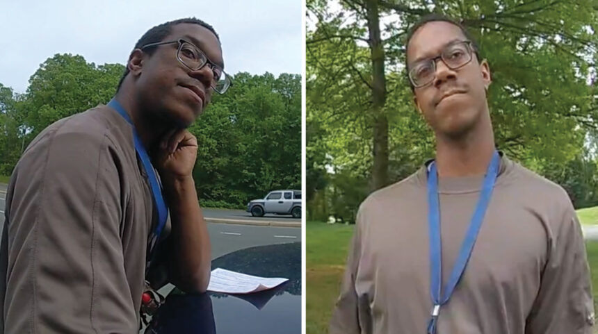 Man with glasses and a blue lanyard outdoors, leaning on a car hood and holding papers near a parking lot trees in the background.